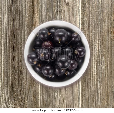 Black currants in a white ceramic bowl. Top view. Ripe and tasty currants on a wooden background.