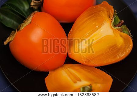 Cut a ripe persimmon in black plate, low key. Sweet, delicious flesh of Persimmon is packed with vitamins, minerals, antioxidants vital for optimum health