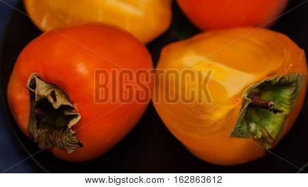 Organic Persimmons in black plate, dark background. These fruits do sweet, tasty treat and have a wealth of health benefits