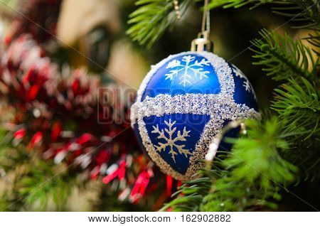 Blue ball with snowflakes surrounded by tinsel on beautiful artificial Christmas tree