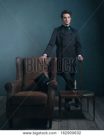 Retro Dickens Style Man Standing With Cane Next To Leather Chair.