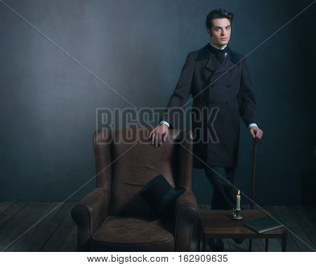 Retro Dickens Style Man Standing With Cane Next To Leather Chair.