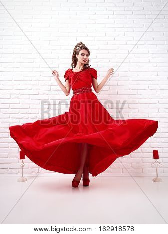 elegant woman in a long flittering red dress is standing in a white room with candles