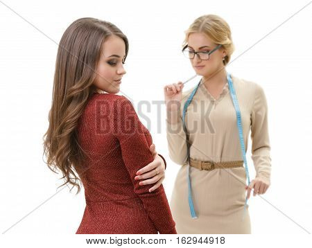 Young sexy dressmaker in slinky beige dress takes measurements of her cute slim long haired client in sexual knitted winy gown studio shot