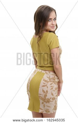 Sexy pretty long haired brunette in slinky printed mustard blouse and mini skirt posing flirty in studio half-turned