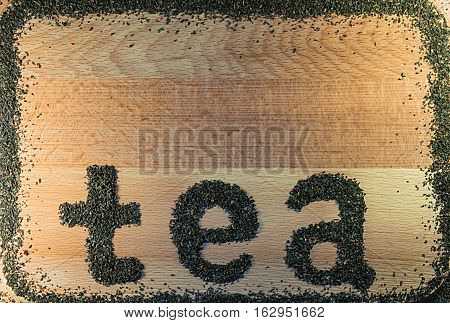 The word tea is laid out on a light-brown wooden Board small leaf black tea. Board is the background. The edges lined with a frame of tea.