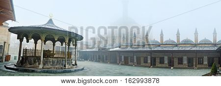 KONYA TURKEY - JANUARY 20 2015: The courtyard of Mevlana Museum with the view on the living chambers of dervishs and the silhouette of the Selimiye Mosque in fog on January 20 in Konya.
