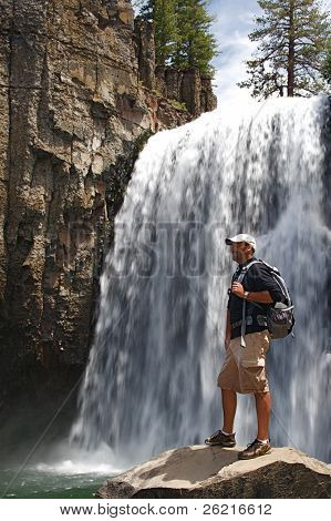 Hiker ทนทานมองภูมิประเทศป่าที่น้ำตกสายรุ้งใน NM Postpile ปีศาจ