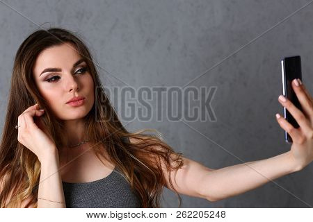 Beautiful European Woman Portrait. Worth A Gray Background Uses A Smartphone Makes Selfie And Reads 