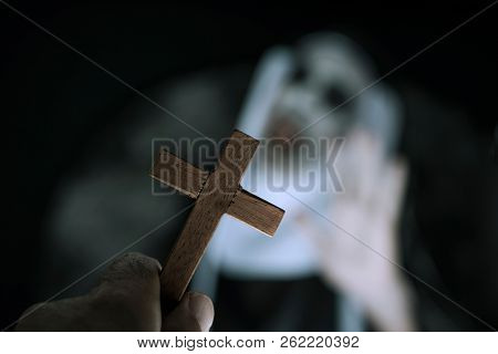 closeup a cross in the hand of a man and a frightening evil nun, wearing a typical black and white habit, screaming