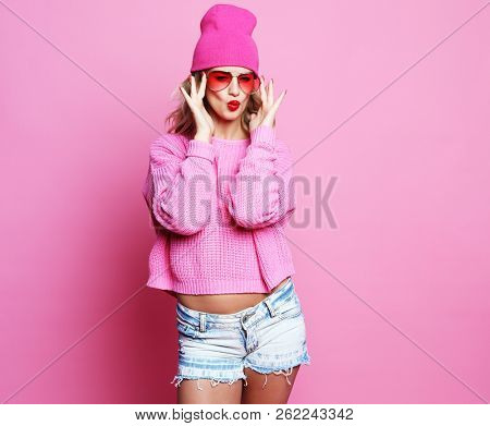 Stylish fashion portrait of trendy casual young woman in pink pulover and hat, posing over pink background.
