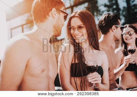 Young Smiling Friends Drinking Wine At Poolside. Group Of Young Happy People Sitting At Poolside Tog