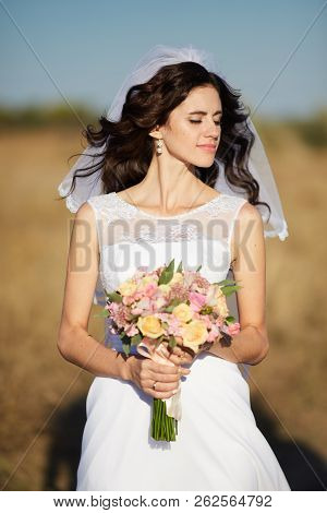 Beautiful Smiling Bride Wearing A Natural Flower Wreath And Standing In The Golden Summer Fields Wit