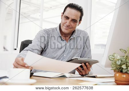Confident Enterpreneur Examining Contract And Using Digital Tablet During Work Day At Office