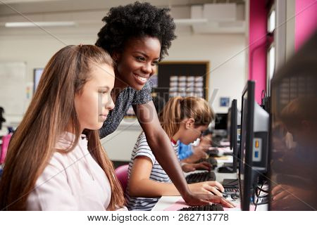 Teacher Helping Female Pupil Line Of High School Students Working at Screens In Computer Class