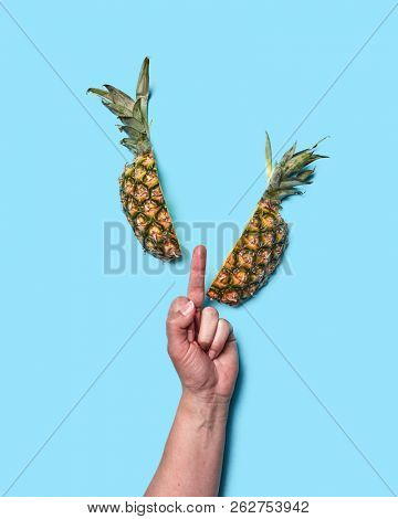 A sign with a woman's hand fucking and a half pineapple on a blue background with space for text. Flat lay