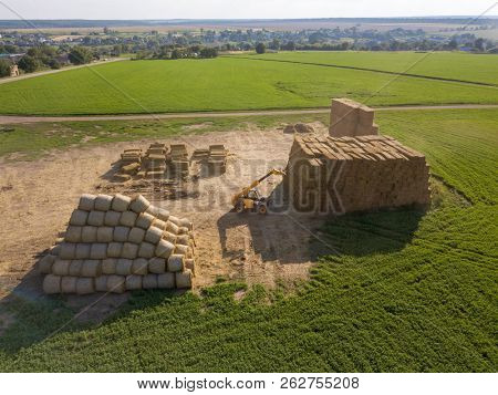 Large haystacks in a field with agricultural machinery tractor against a blue sky on a sunny day