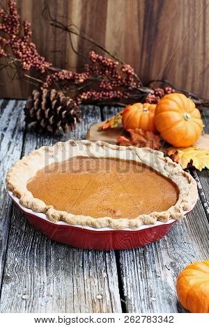 Homemade Pumpkin Pie In Red Ceramic Pie Plate Over A Rustic Wooden Background. Extreme Shallow Depth