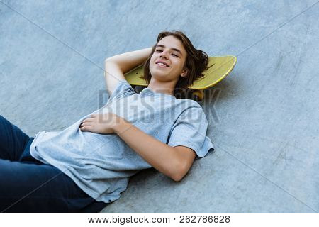 Happy young teenge boy spending time at the skate park, laying on a skateboard at a ramp