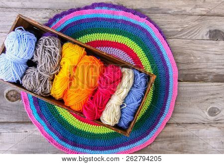 Knitted Striped Mat And Colorful Skeins Of Wollen Yarn On Wooden Background.