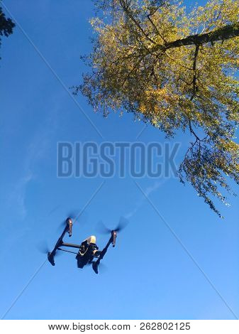 Kopter (drone) Flying In The Blue Sky, Propellers Rotate, Leaves And Treetops Are Visible