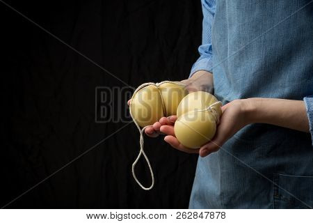 Gourmet Italian Cheese Scamorza In Hands Of Cheese Maker In Blue Apron On Black Background