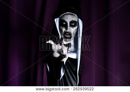 closeup of a frightening evil nun, wearing a typical black and white habit, peeping out from a purple curtain