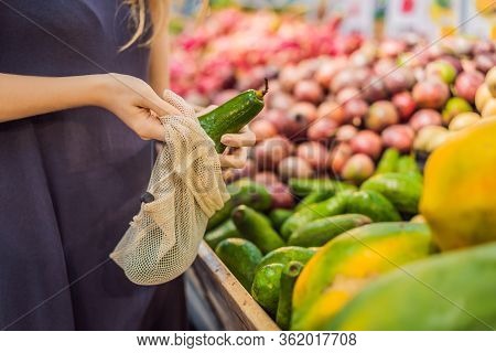 Woman Chooses Avocado In A Supermarket Without Using A Plastic Bag. Reusable Bag For Buying Vegetabl