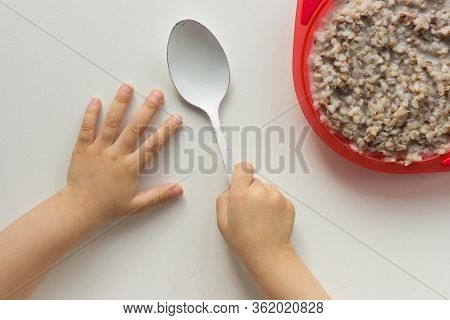 Top View Of Child Hands Holding Spoon In Right Hand And Buckwheat Porridge On White Background