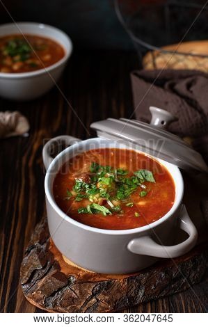 Bean Soup With Meat And Vegetables Served On A Rustic Board And Wooden Table With Bread And Garlic. 