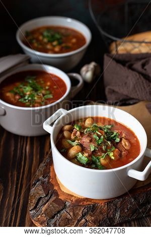 Bean Soup With Meat And Vegetables Served On A Rustic Board And Wooden Table With Bread And Garlic. 
