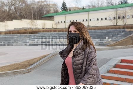 Woman Of European Appearance In A Black Medical Mask On Her Face From Coronavirus Looks At The Backg