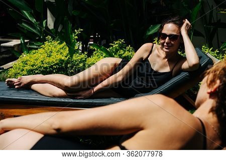 Two Relaxing Young Women Lying Under A Tropical Sun On Deck Chairs