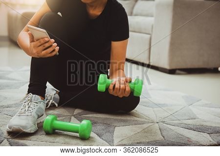 A Sporty Woman Using Smartphone During Workout At Home In The Living Room. Online Personal Trainer O