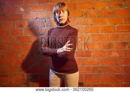 A Middle-aged Woman Poses Showing Clothes Near Red Brick Wall. An Inept Model In An Inept Shoot