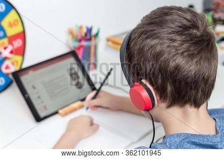 Eight Years Old Boy Behind The Table Study At Home Using A Tablet And Headphones, Digital Education,