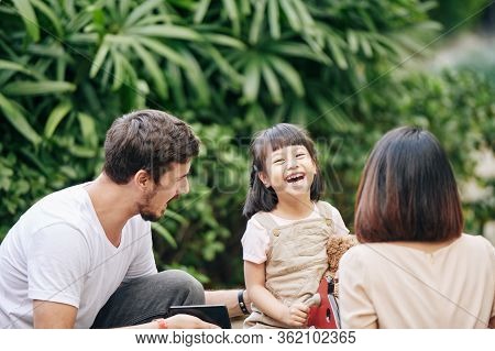 Happy Little Mixed-race Girl Enjoying Speding Time With Parents In Park
