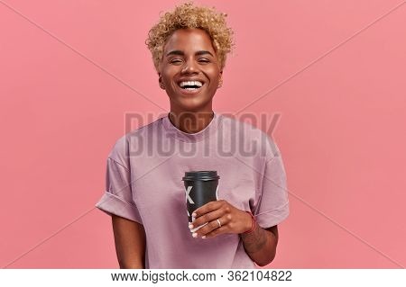 Happy Optimistic Dark Skinned Woman Gestures Actively, Drinks Hot Beverage, Talks Emotionally With F
