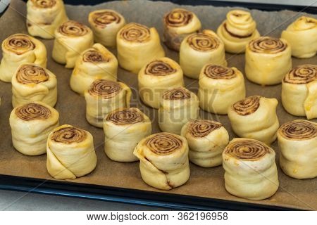 The Preparation Of The Rolls Or Buns With Cinnamon And Sugar. Raw Rolled Rolls Stand On Baking Paper