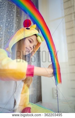 Little Girl In Kigurumi Unicorn Draws The Rainbow On The Window. Stay Home. Flashmob Chasetherainbow
