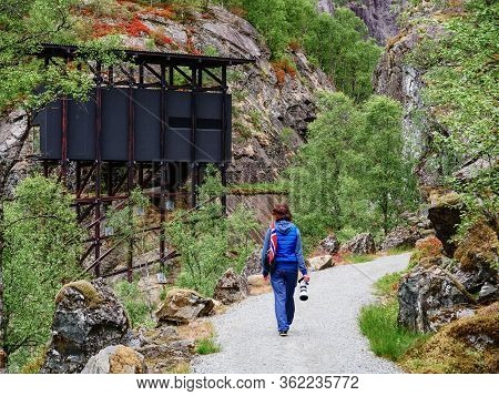 Tourist Woman With Norwegian Flag And Camera Walking Trough Mountains Path In Allmannajuvet Area Sau