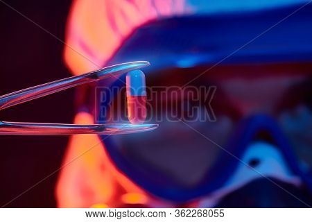 COVID-19 or 2019-nCoV. Close-up portrait of a scientist microbiologist in a protective PPE suit showing the capsule with a vaccine against coronavirus. Vaccination.