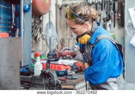 Woman mechanic working with disk grinder on piece of metal