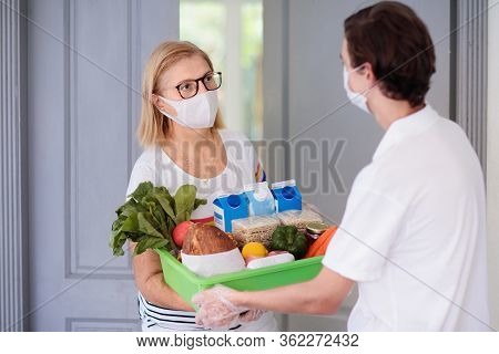 Food Delivery During Corona Virus Outbreak. Courier Wearing Face Mask Delivering Grocery Order In Co