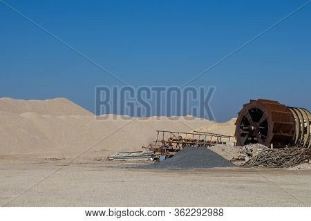 Hills Of Gravel At A Minining Plant. Rusted Machines For The Extraction In The Foreground. Bright Bl