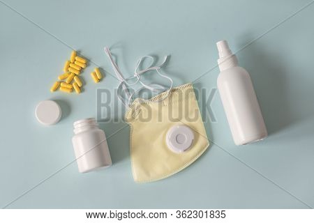 Yellow Face Mask With A Respirator On A Light Blue Background, Next To Hand Sanitizer And Natural St