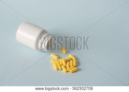 A White Open Jar Lies On Its Side Against A Blue Background And Yellow Pills Are Scattered. Alternat