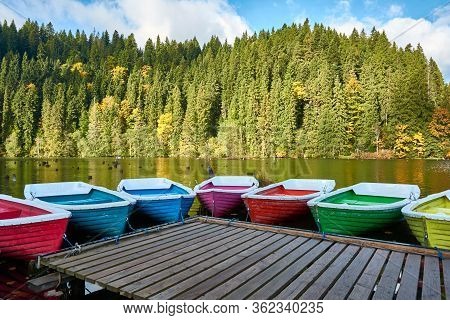 Multi-colored Boats At The Pier On Lake Lacu Rosu, Romania. Autumn Landscape Of Mountain Lake, Fores