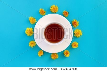 Cup Of Herbal Tea Over Blue Paper  Background Decorated With Yellow Dandelions Flowers And Green Lea