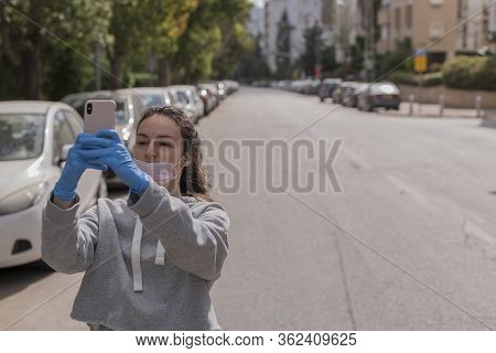 Young Beautiful Girl Takes A Selfie On An Empty Street. No People. She Is Wearing Protective Gloves 